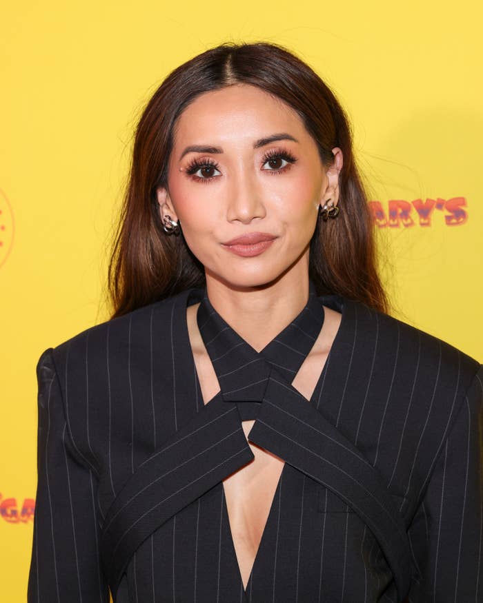 Person successful  a achromatic  structured outfit with intersecting straps, posing astatine  an lawsuit   against a yellowish  background