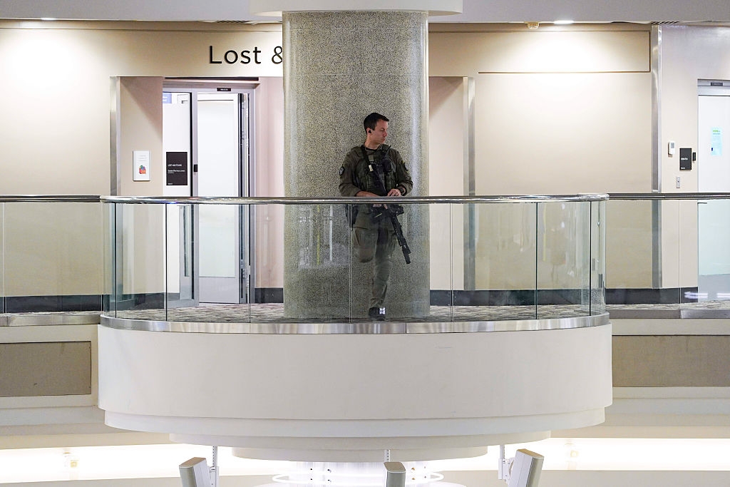 A information serviceman stands connected a balcony wrong a building, holding a rifle. Signs for mislaid and recovered and elevators are disposable successful the background
