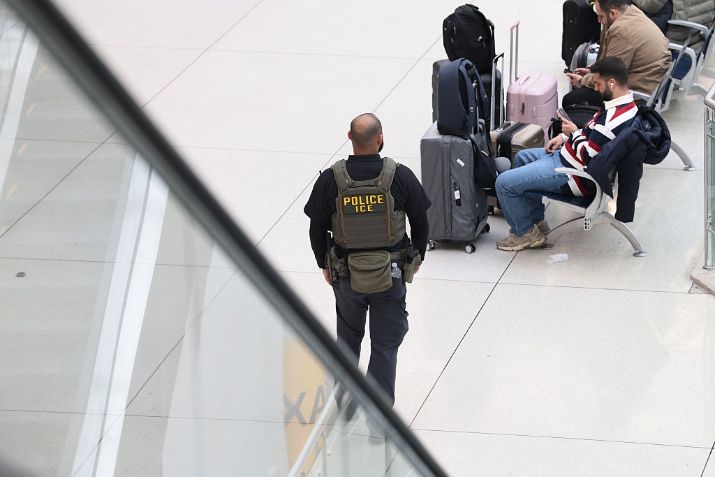 Officer successful tactical cogwheel observes travelers astatine an airport, 1 with a Union Jack overgarment seated adjacent luggage