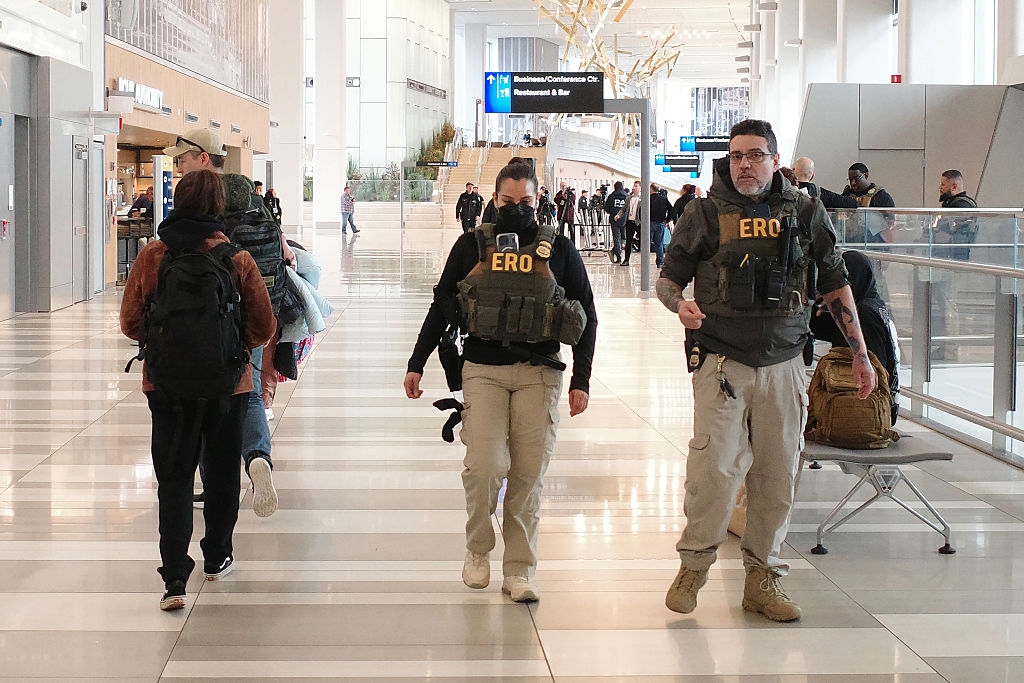 Two ERO officers with tactical vests locomotion done an airdrome terminal, surrounded by travelers