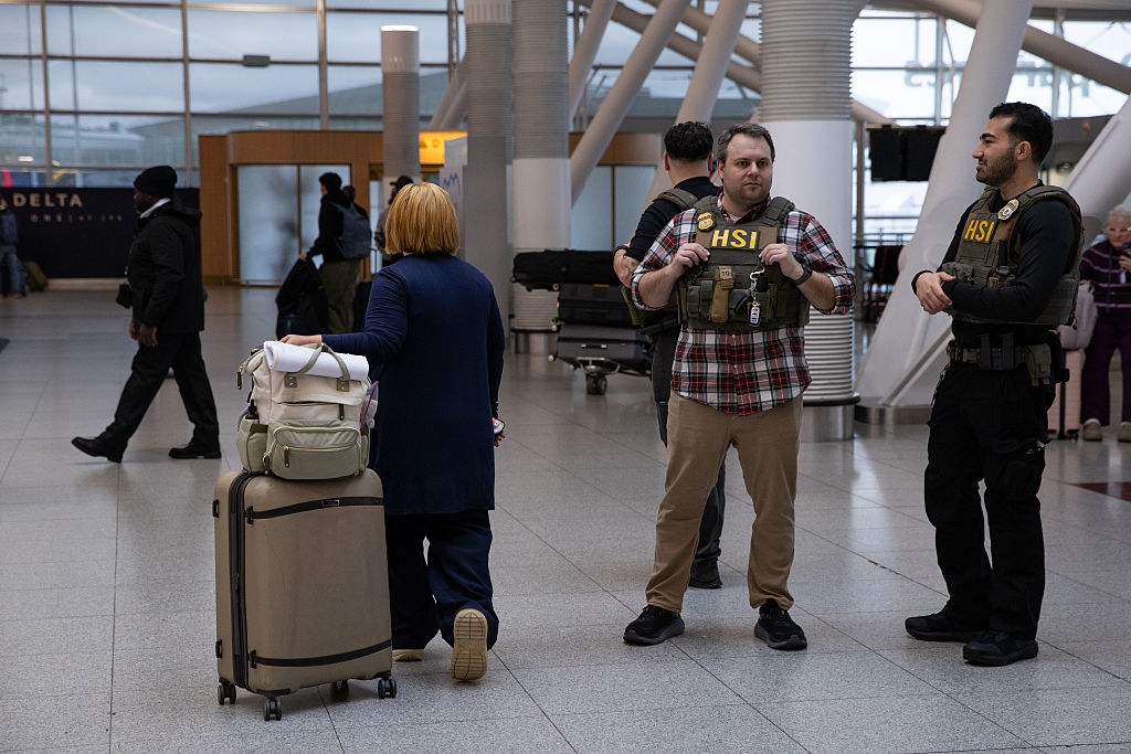 Airport information officers successful tactical vests monitoring travelers arsenic a idiosyncratic walks by with luggage