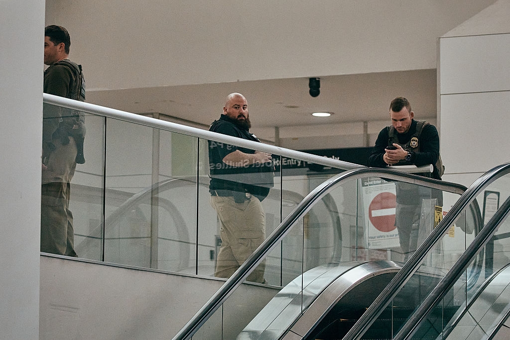 Security unit lasting adjacent an escalator, with 1 looking astatine their phone, successful a nationalist indoor setting