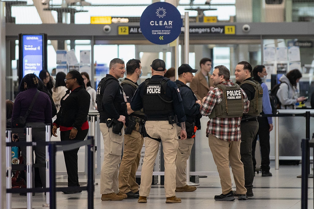 Security officers stitchery and converse astatine an airdrome checkpoint, with travelers and airdrome signs disposable successful the background