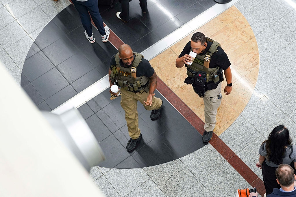 Two constabulary officers successful tactical vests patrol an airdrome terminal, holding java cups, seen from above