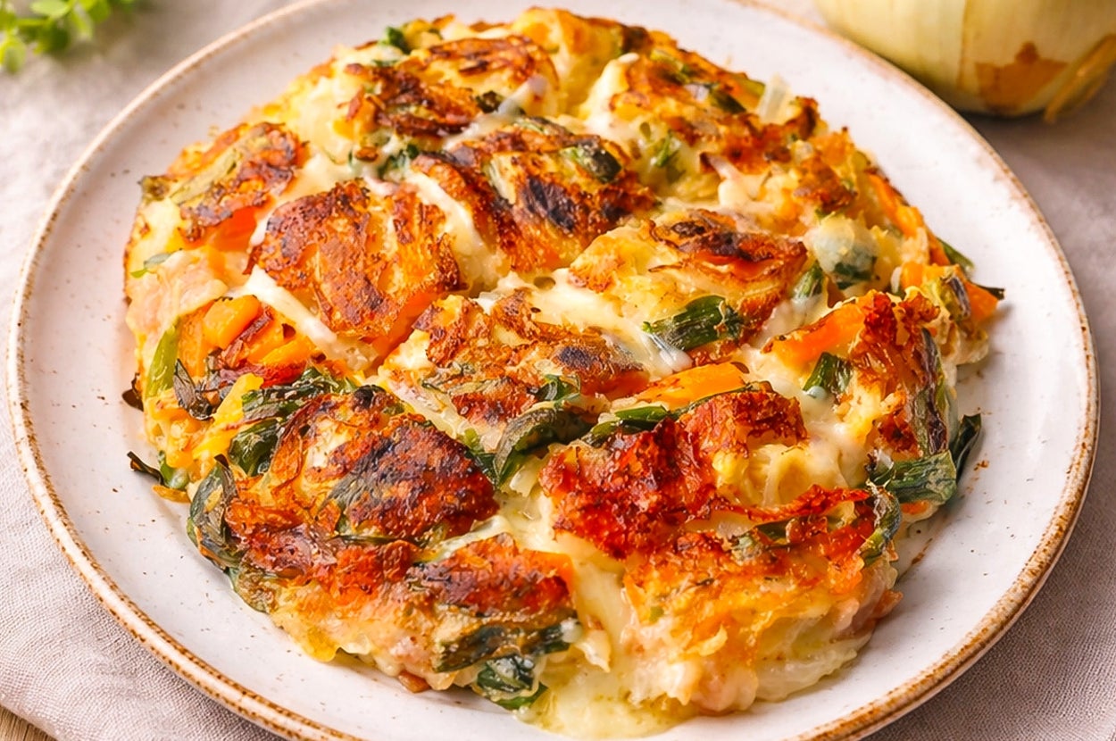 おいしそうなオムレツ風の料理が皿に盛られ、背景に玉ねぎと緑の枝がある。