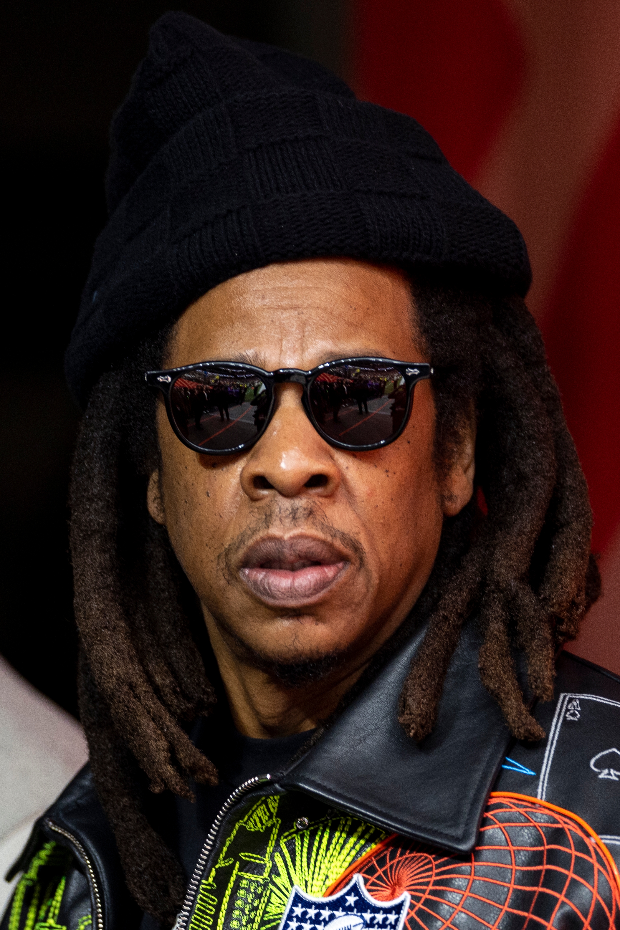 Person wearing sunglasses, hat, and leather overgarment   with unsocial   patterns