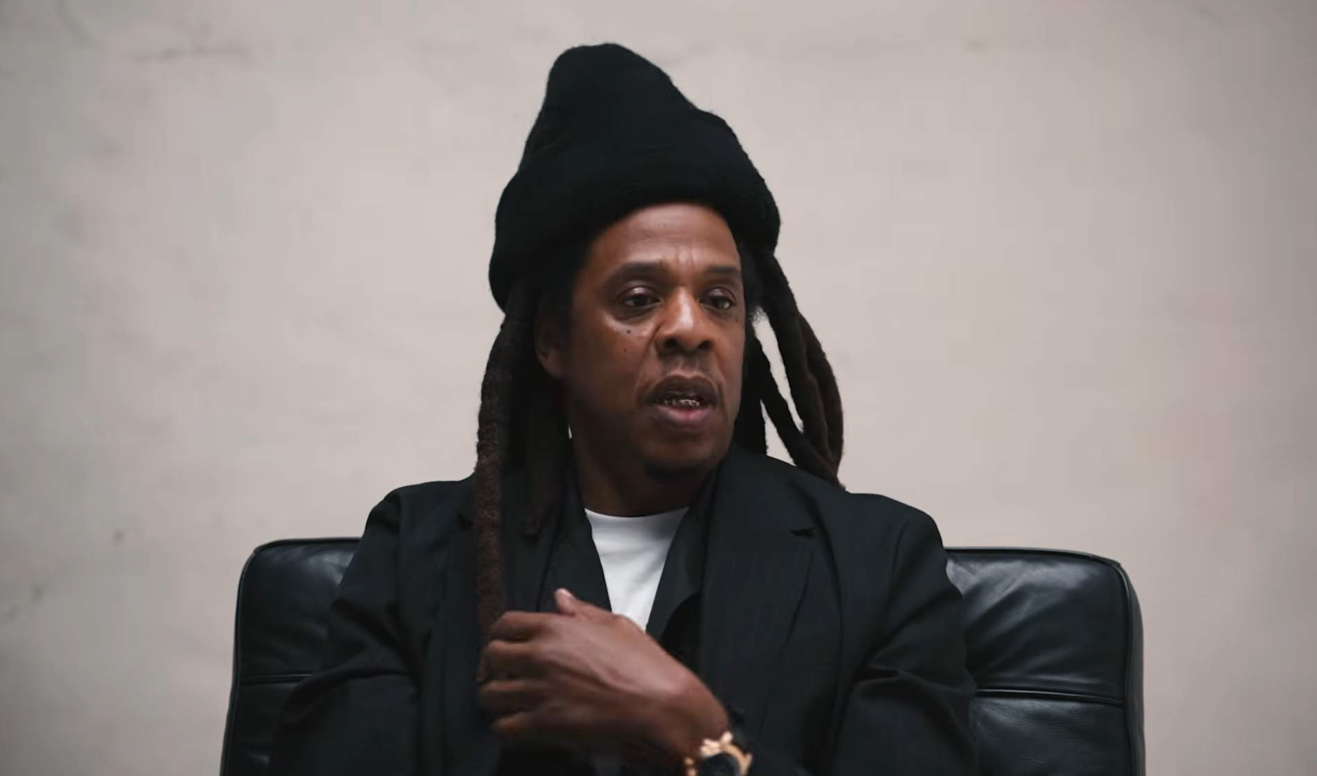 Person successful  a achromatic  overgarment  and chapeau  sitting connected  a chair, gesturing with 1  hand