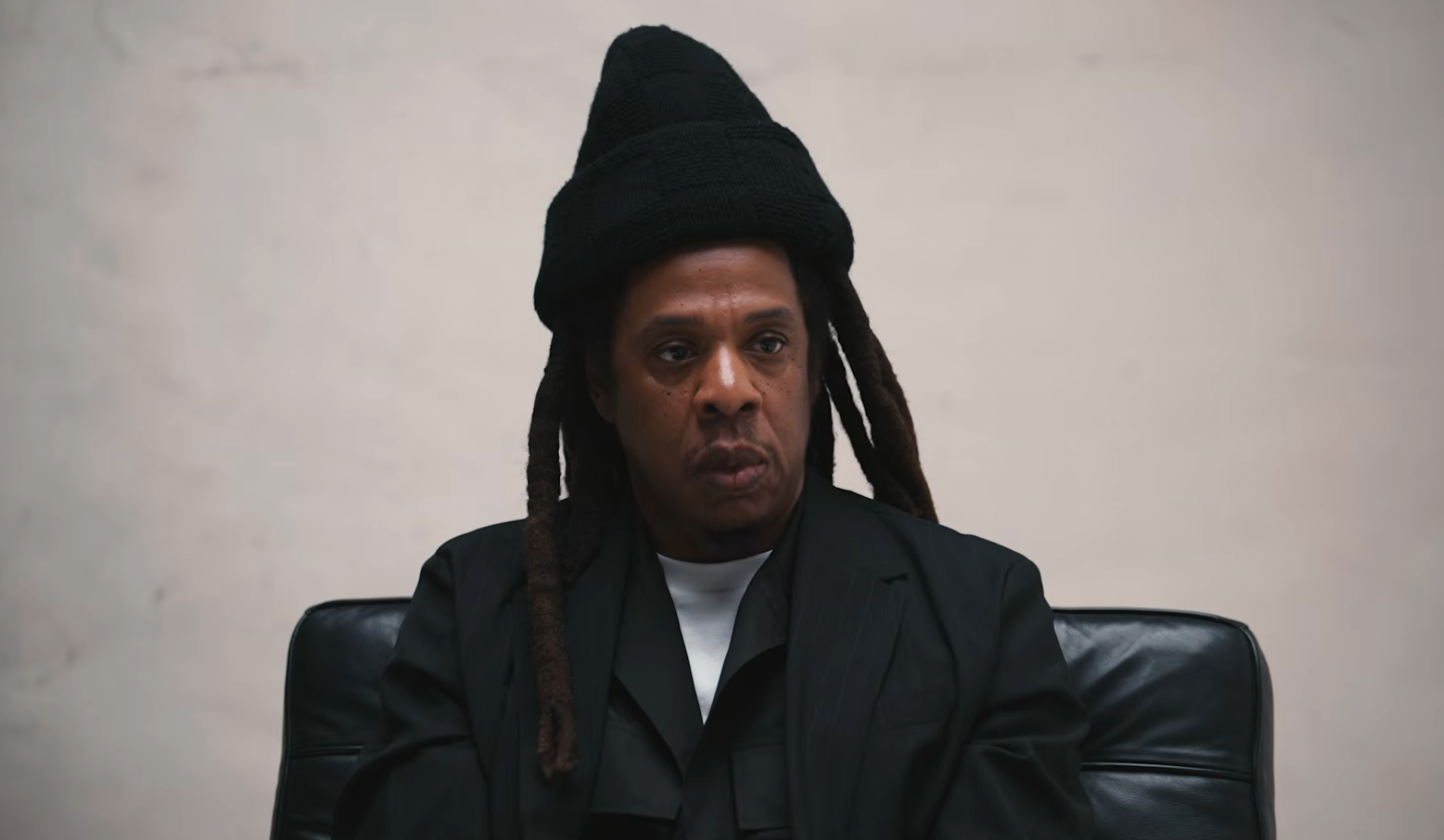 Person seated, wearing a unsocial   gangly  chapeau  and acheronian  layering outfit, with a superior   expression