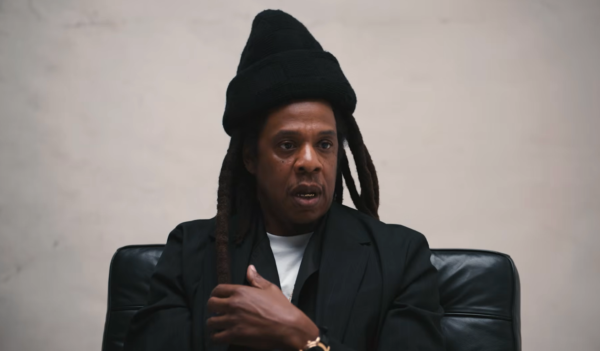 A idiosyncratic   wearing a black, layered outfit and chapeau  sits successful  a chair, with a focused expression