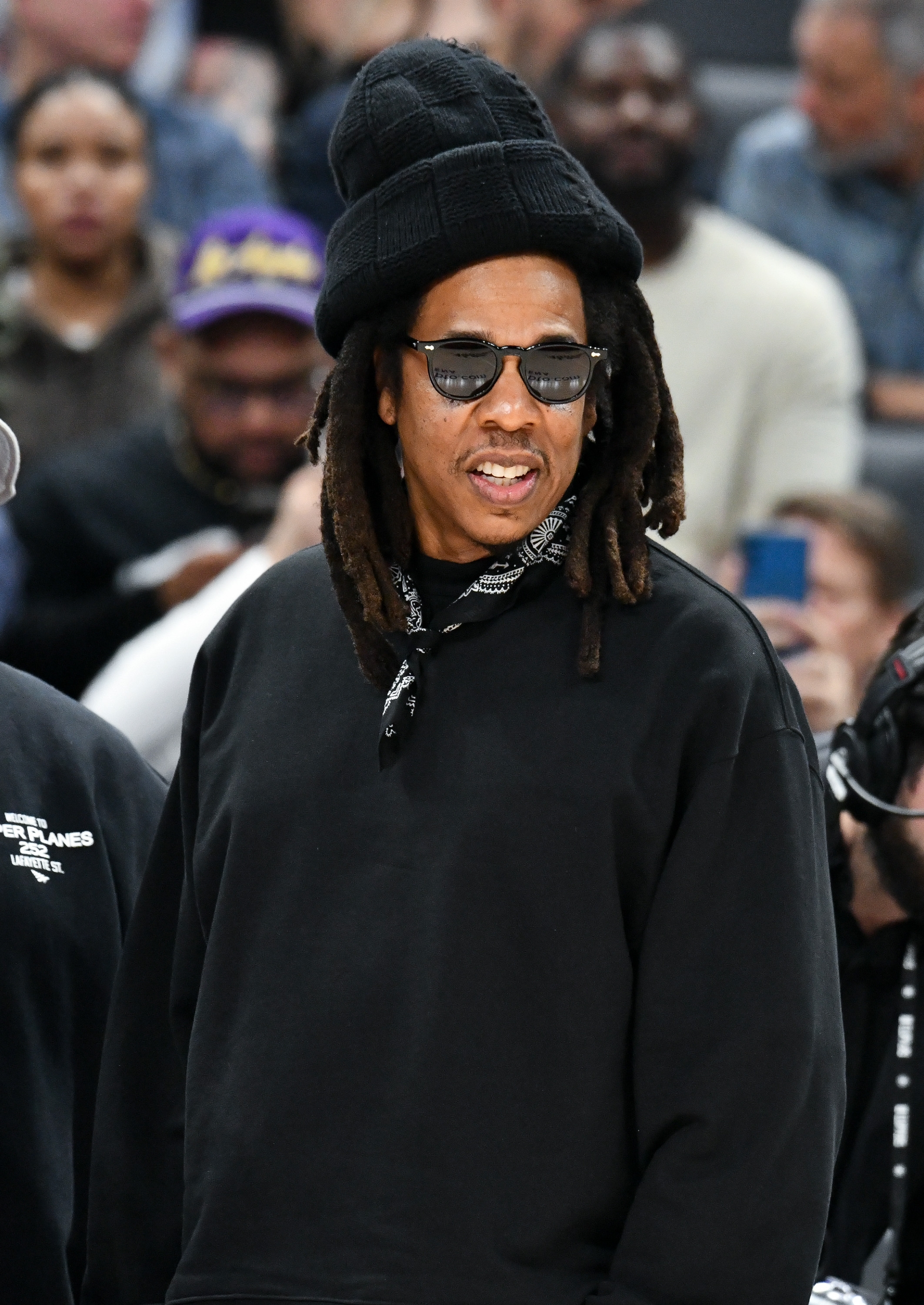 Person with dreadlocks and sunglasses wears a layered chapeau  and a achromatic  sweatshirt with a bandana scarf astatine  a nationalist   event