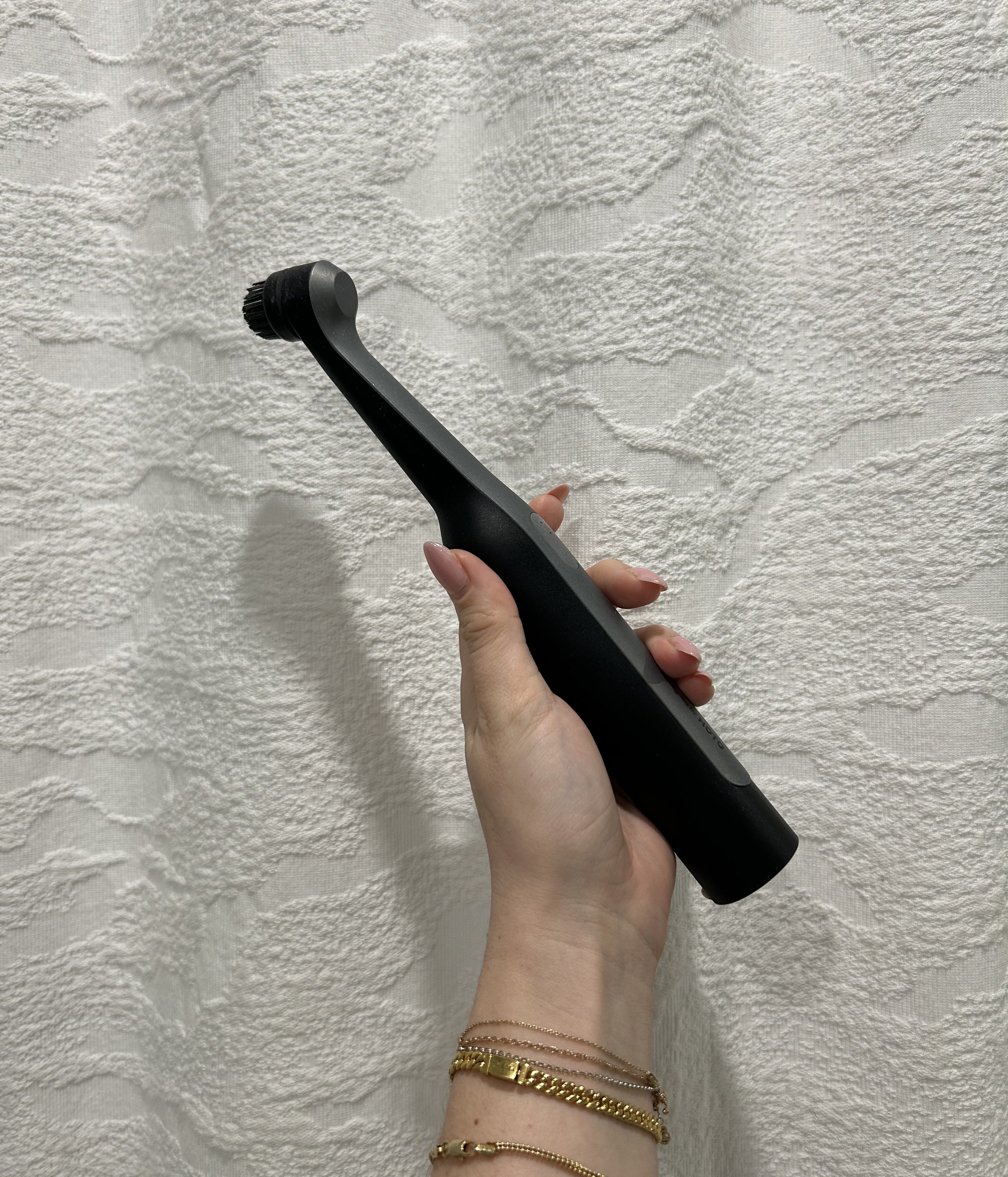 Hand holding a sleek electric toothbrush against a textured background, displaying its modern design