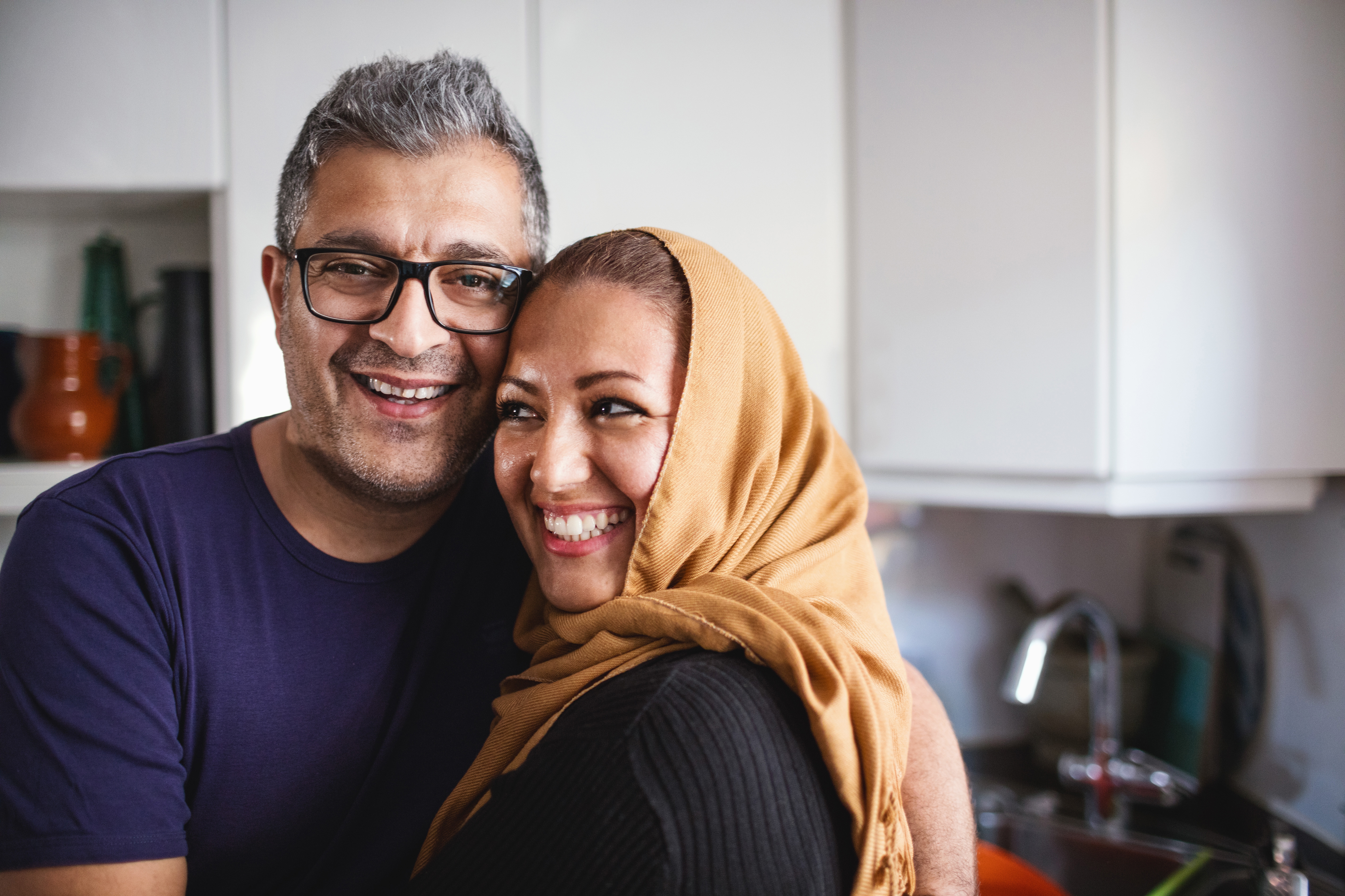 A smiling couple embraces in a cozy kitchen, radiating warmth and affection