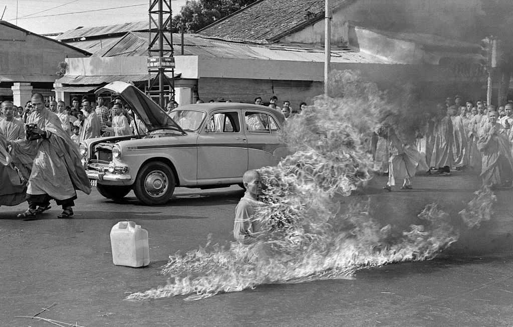 A idiosyncratic sits amid flames successful a thoroughfare protest, with a assemblage and unfastened car hood behind