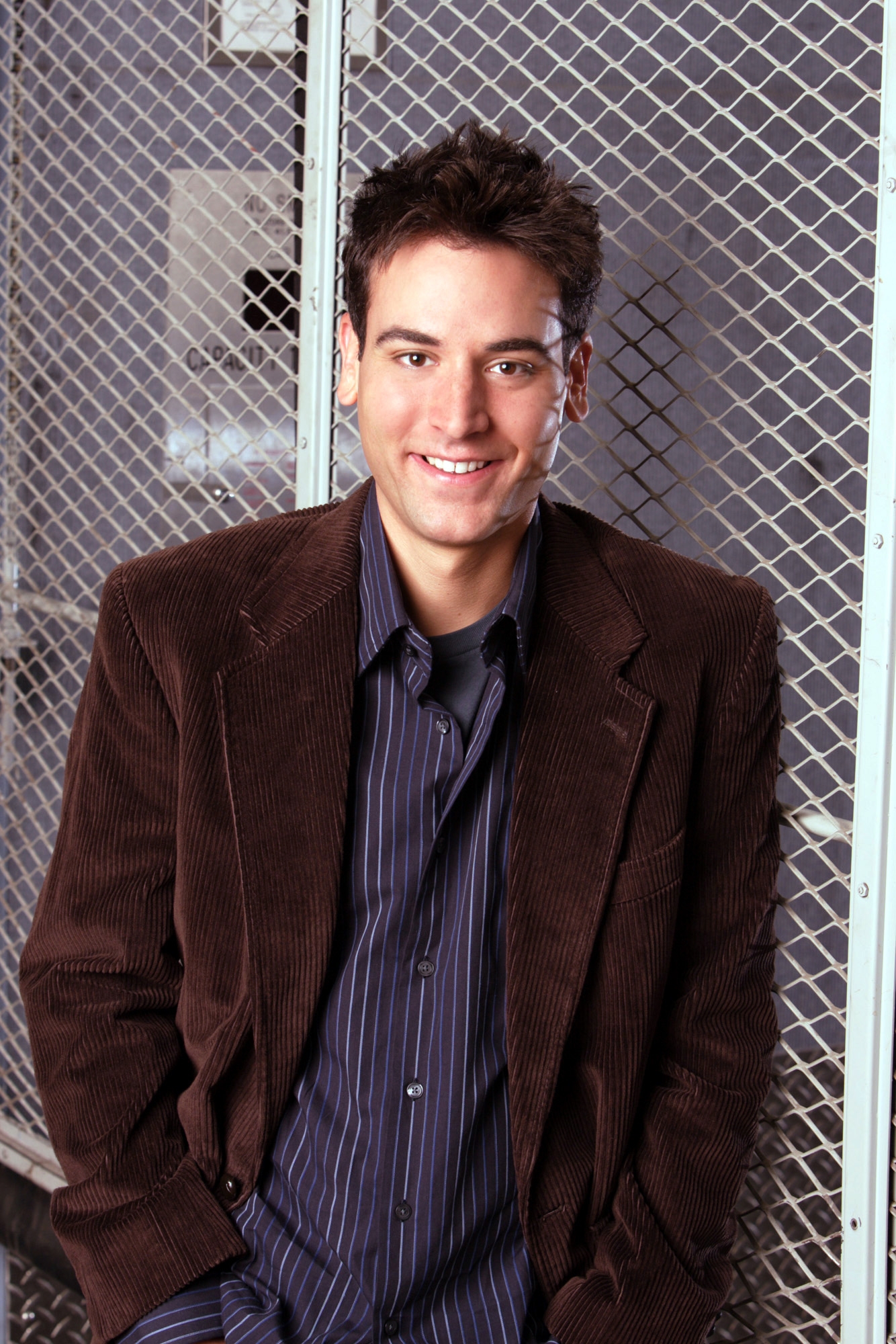 Person successful  a corduroy blazer and striped garment  stands smiling successful  beforehand   of a metallic  grid backdrop