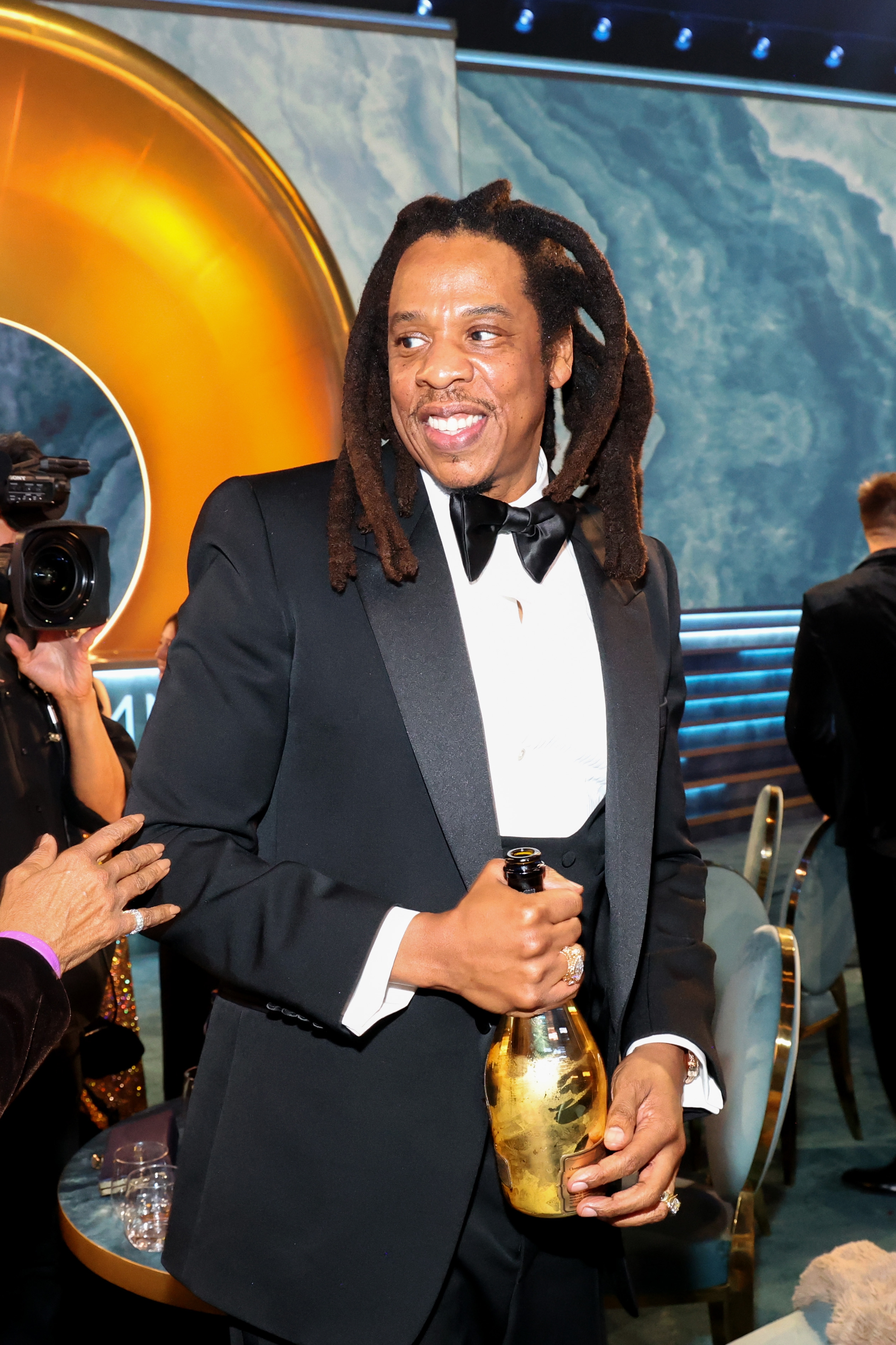 Man successful  a tuxedo holding a champagne vessel  astatine  a ceremonial  event, smiling and interacting with others