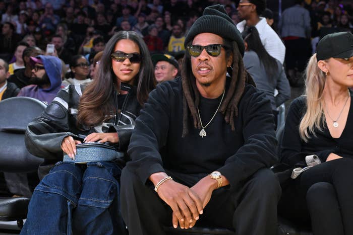 Two radical   sitting courtside astatine  a hoops  crippled  wearing casual, stylish outfits with sunglasses and hats