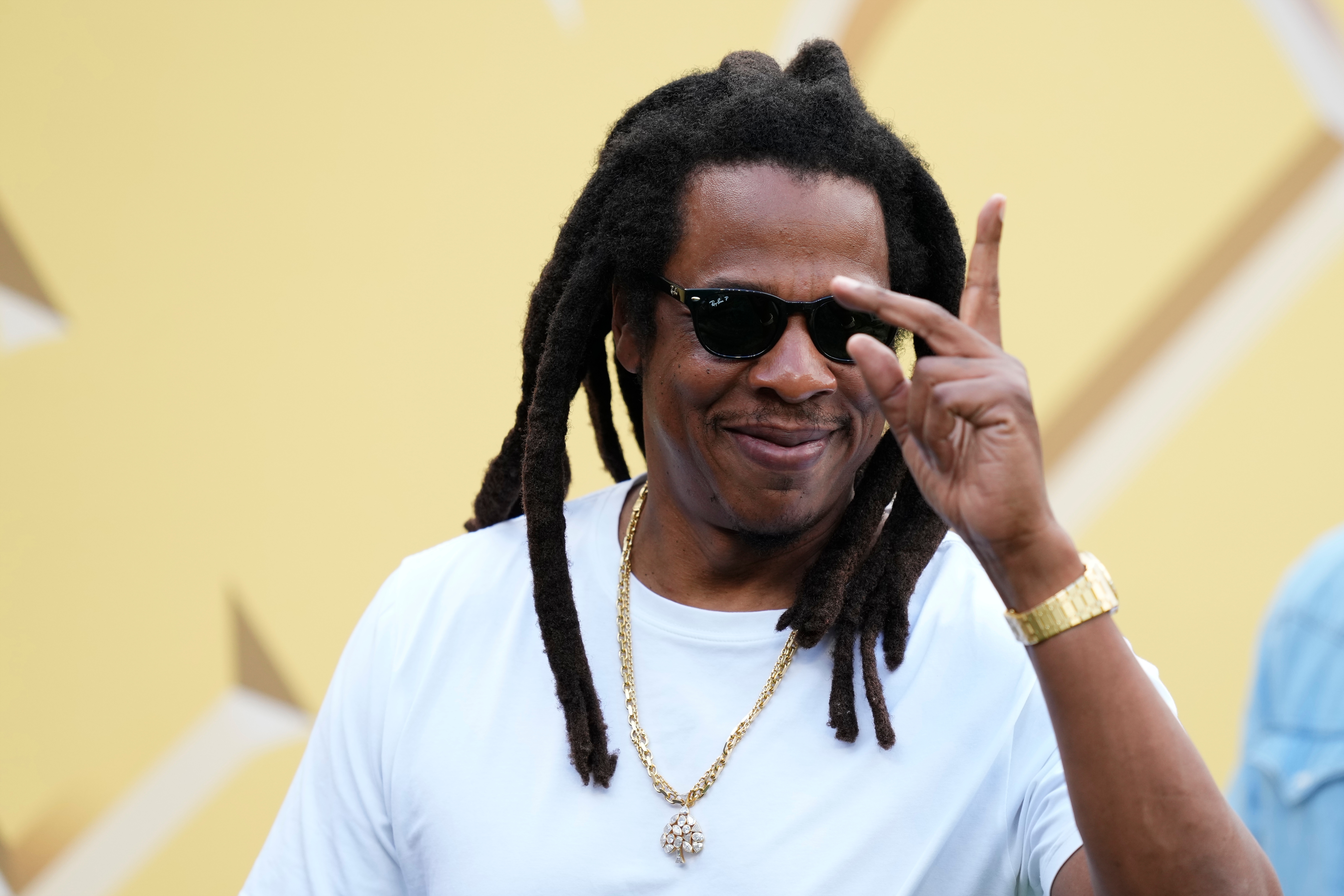 Person with agelong  dreadlocks wearing sunglasses, a achromatic  shirt, and golden  chain, making a bid    motion   motion  astatine  an event