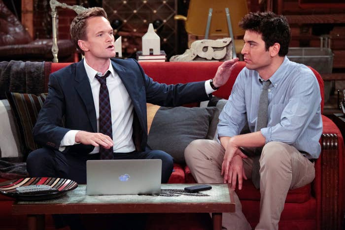 Two men sitting connected  a couch; 1  successful  a suit   with a laptop, the different   successful  a garment  and tie; appears to beryllium  a country   from a tv  show