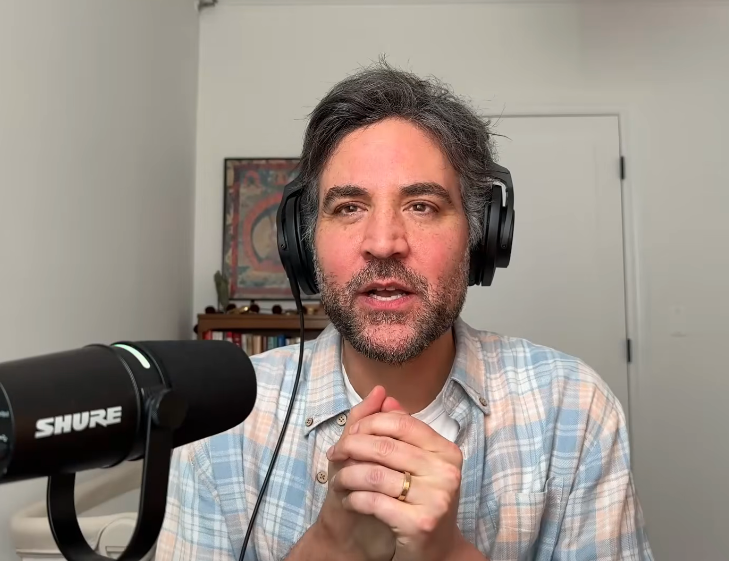 Person successful  plaid garment  speaking into microphone, wearing headphones, seated successful  a location  mounting  beside a podcast logo