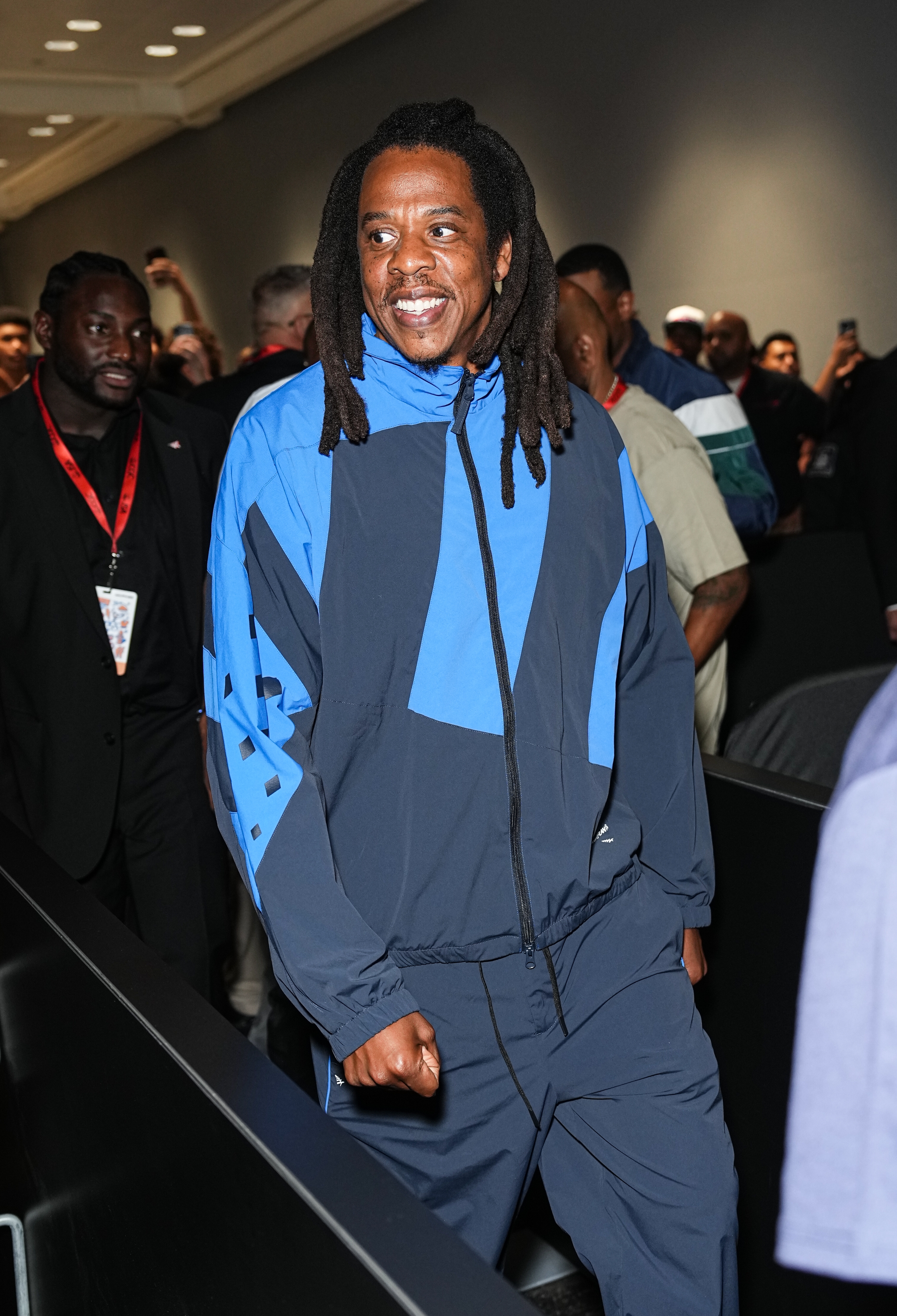 A idiosyncratic   with agelong  hairsbreadth  smiles portion    walking, wearing a stylish, casual tracksuit. The inheritance  features radical   and a dimly lit room