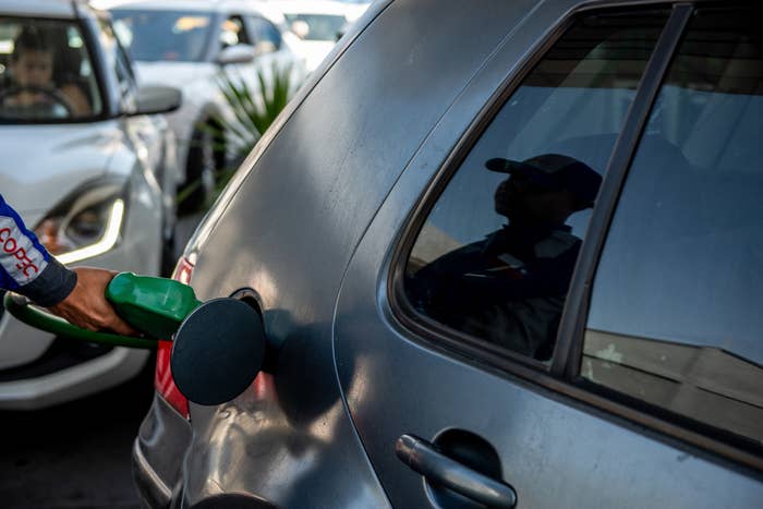 Person refuels a parked car   with a pump astatine  a state  station; reflection   disposable   connected  car   window