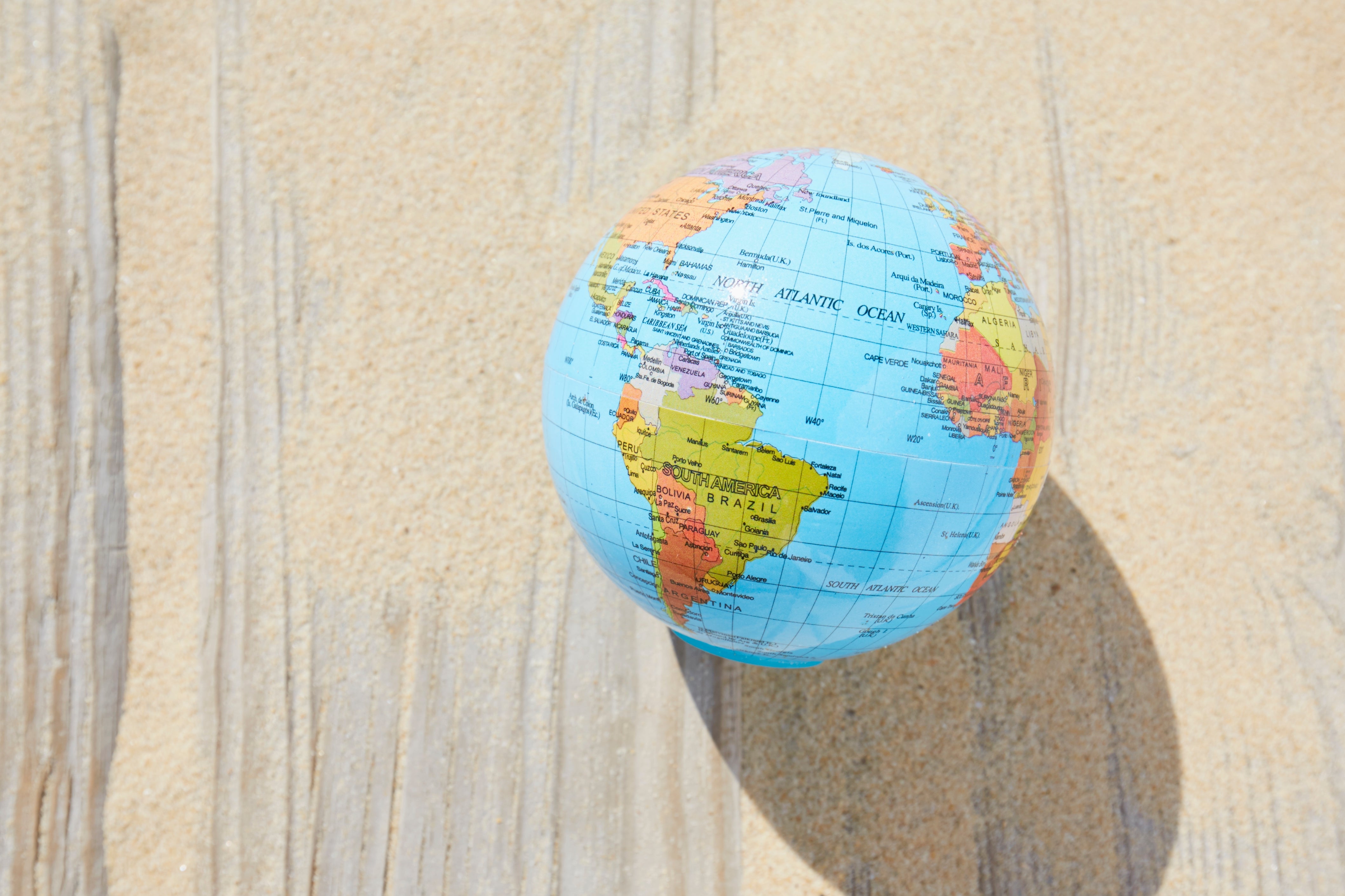 A small globe rests on a sandy surface, symbolizing travel and exploration