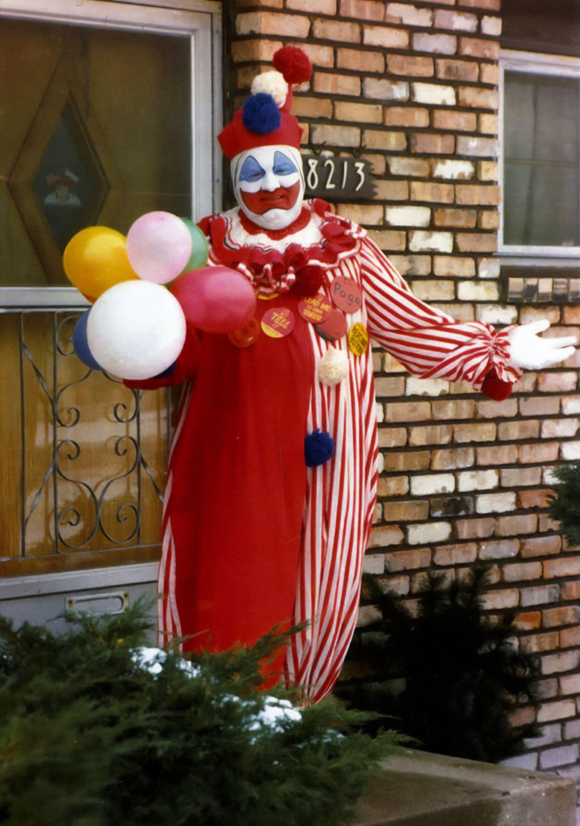 Clown successful a reddish and achromatic striped costume holds colorful balloons and smiles successful beforehand of a ceramic house