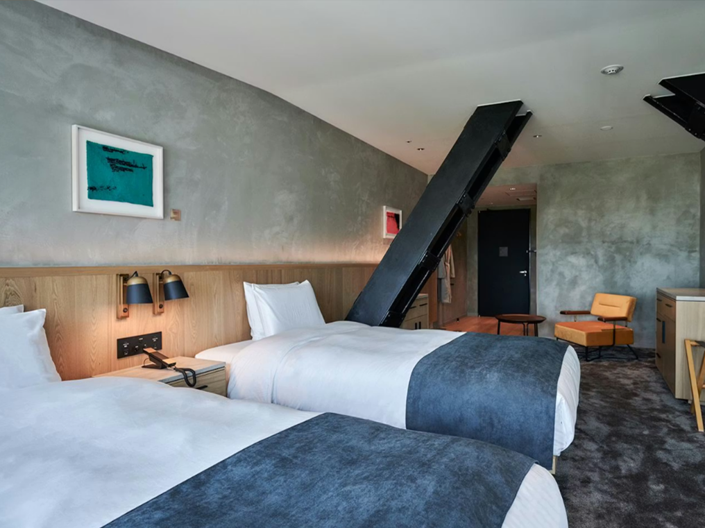 モダンなホテルの客室。2台のベッド、アームチェア、小さなテーブルが配置されています。シンプルで洗練されたデザイン。