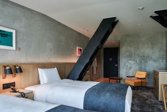 モダンなホテルの客室。2台のベッド、アームチェア、小さなテーブルが配置されています。シンプルで洗練されたデザイン。