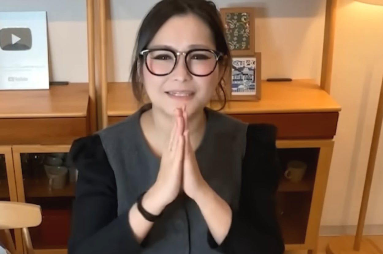 女性がテーブルに座り、手を合わせて「いただきます」と挨拶しています。後ろには賞やランプが置かれています。