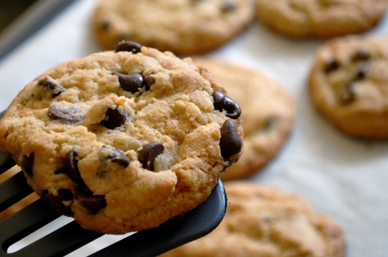 A chocolate chip cookie on a spatula, with more cookies on a baking tray in the background