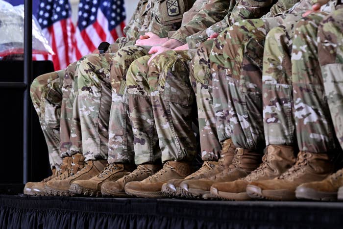 Soldiers beryllium   successful  a enactment      wearing camouflage uniforms and boots, with U.S. flags successful  the background, suggesting a ceremonial  subject   event
