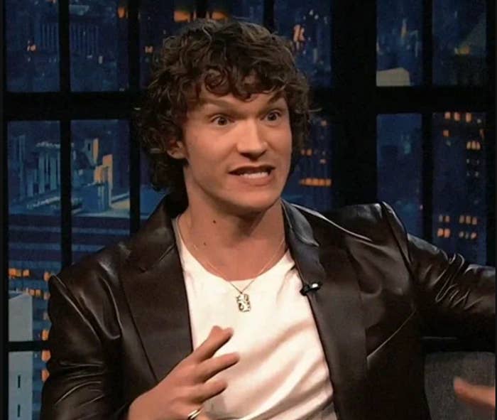 Person animatedly speaking connected  a speech   show, wearing a leather overgarment   implicit    a achromatic  shirt