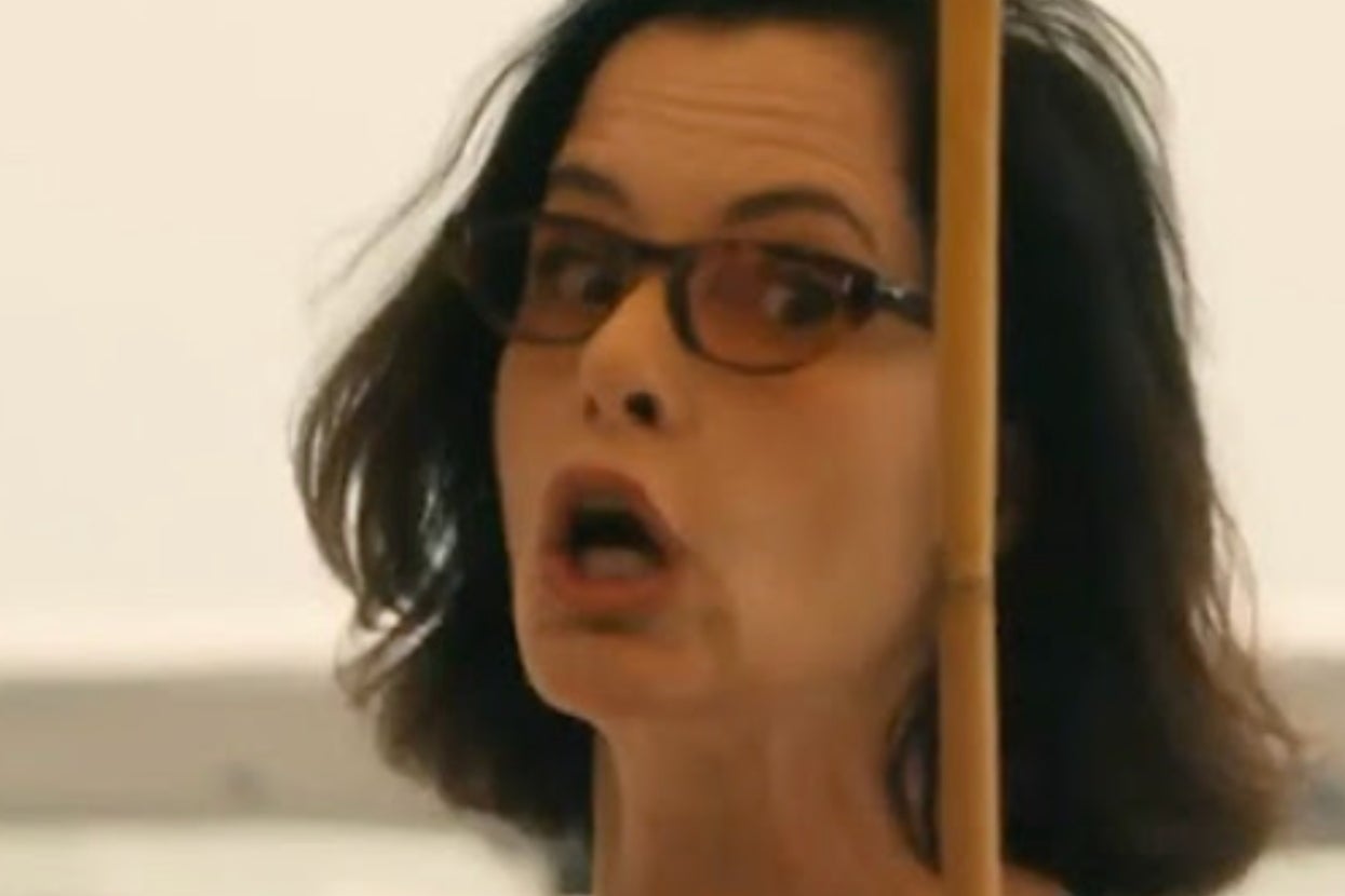 A person with sunglasses holds a stick while speaking with an intense expression in a TV or movie scene