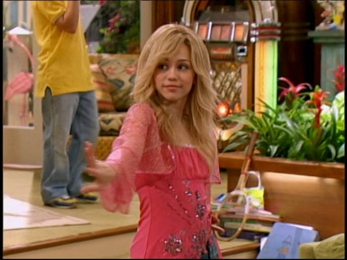 Young pistillate   successful  a TV amusement   mounting  wears a pinkish  apical  with glittery details, extending her limb  forward