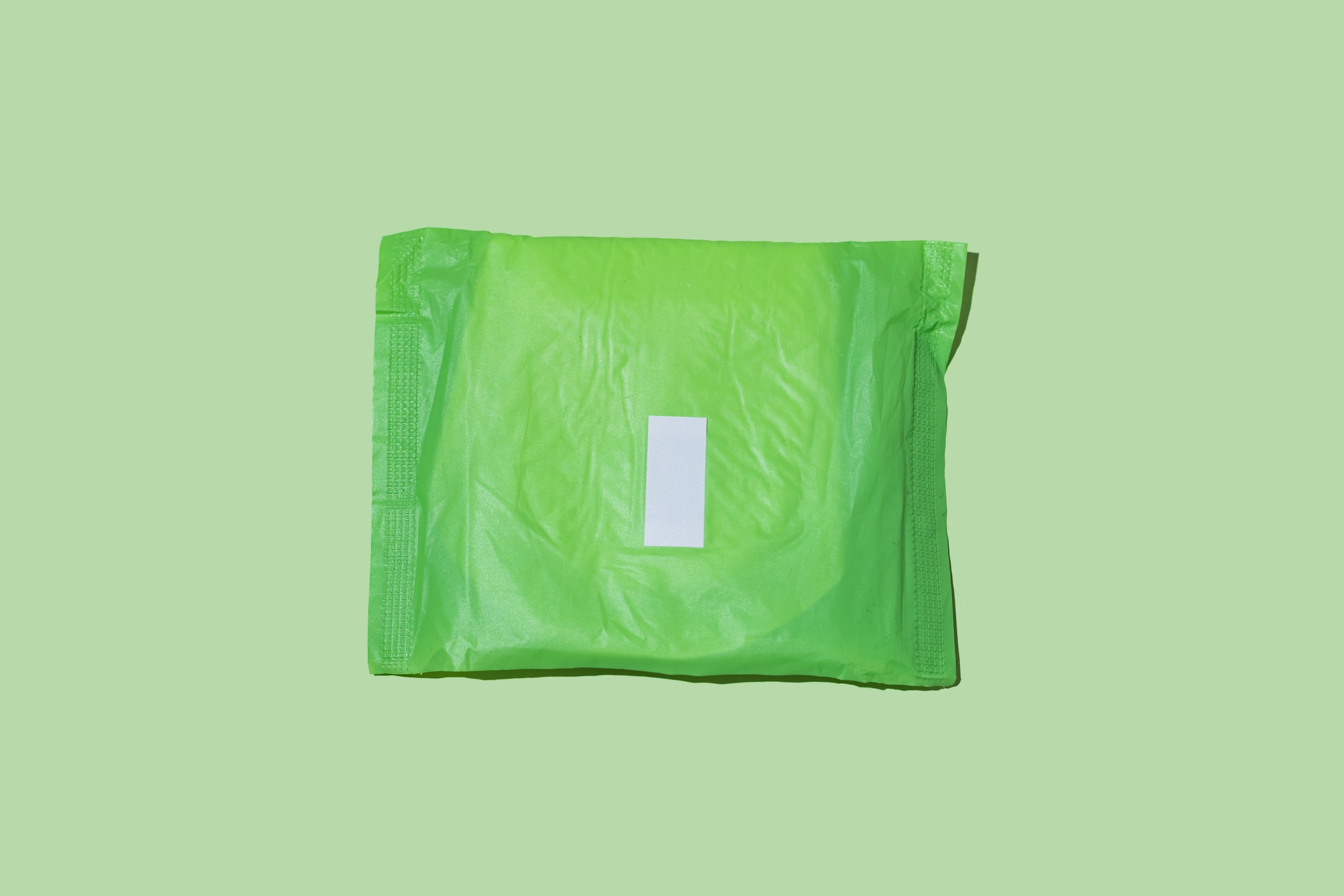 Sanitary pad in green wrapper, lying on a flat surface, symbolizing personal hygiene and menstrual health topics