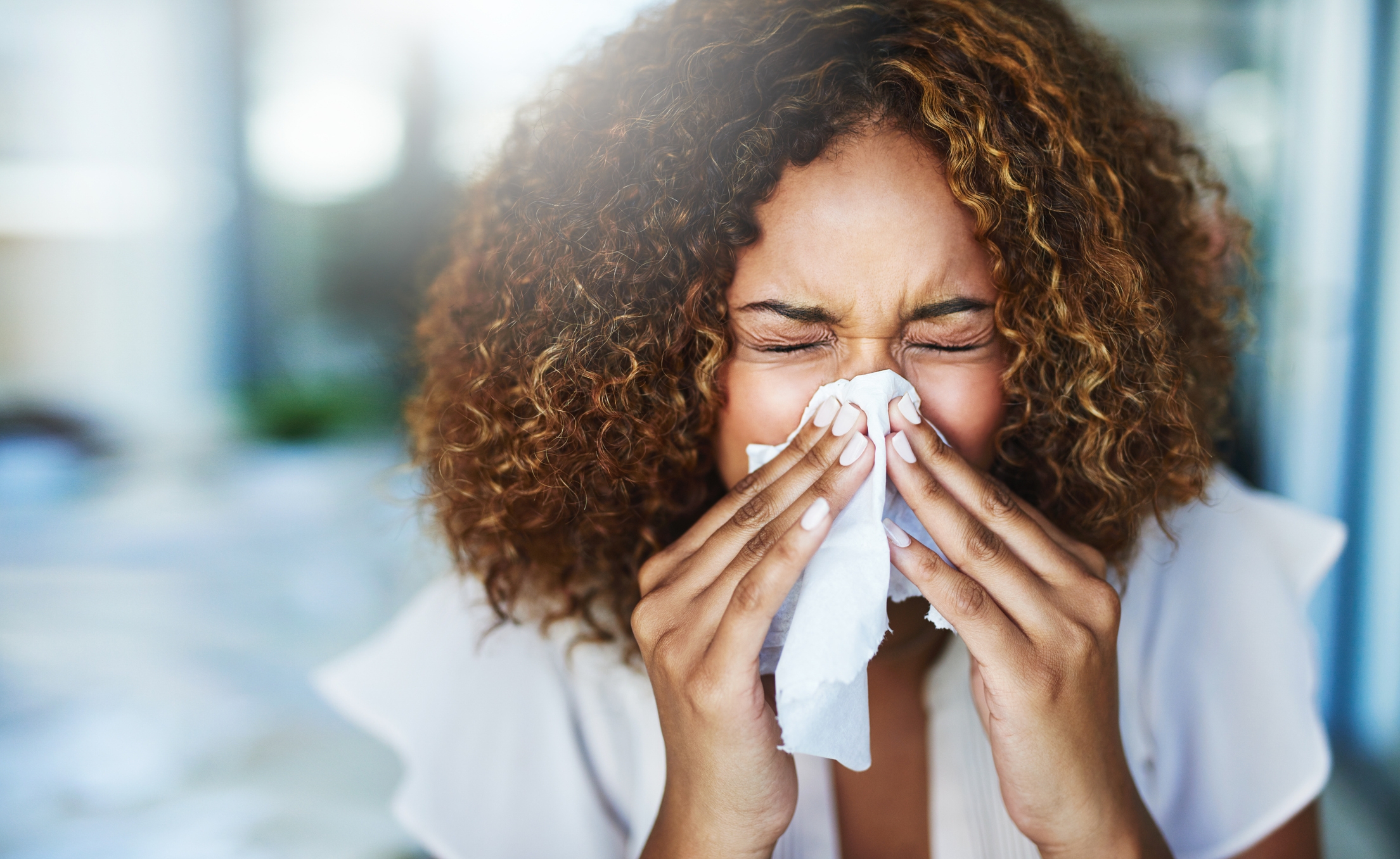 Woman sneezes into tissue, closing her eyes and scrunching her face