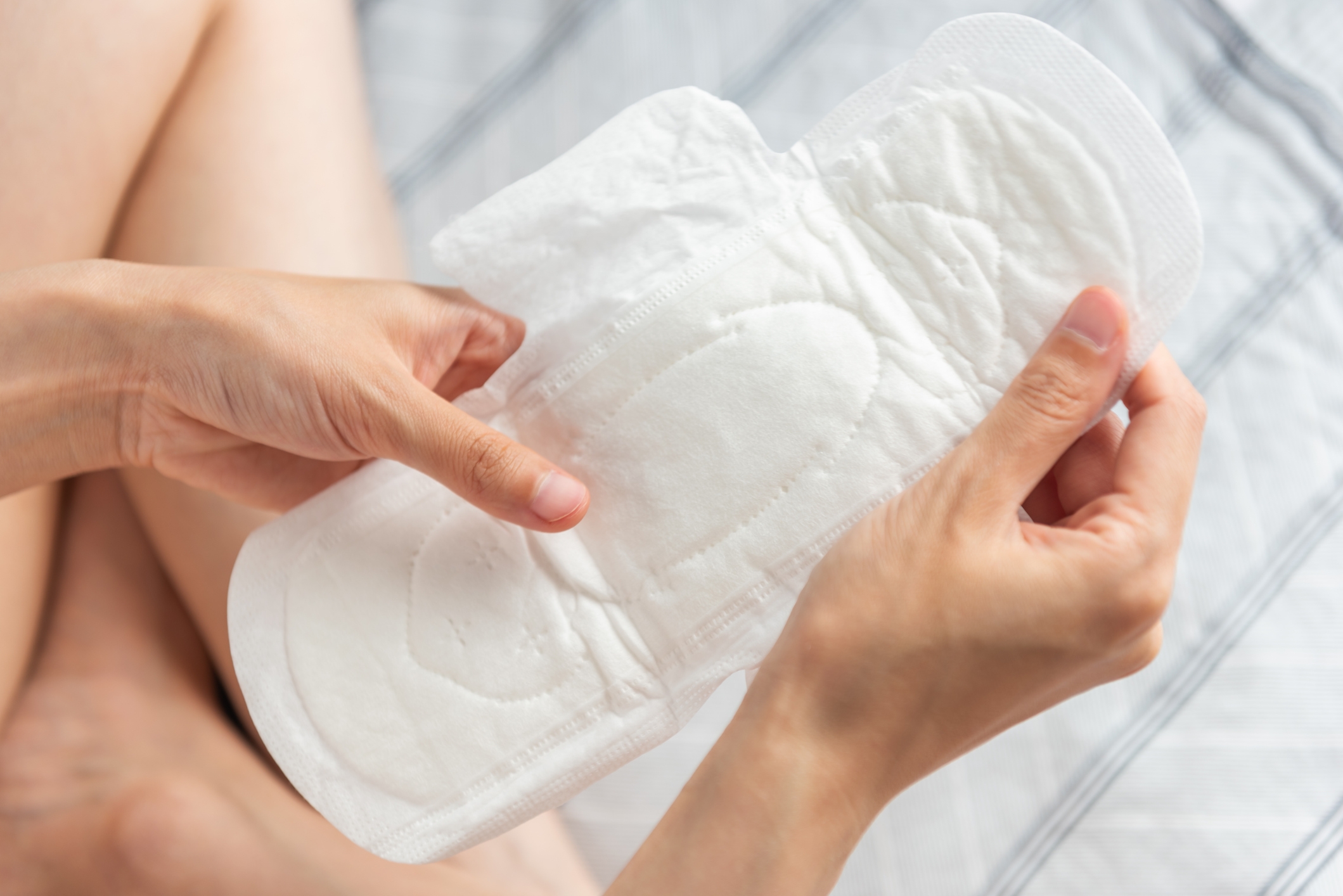 Hands holding an open sanitary pad, suggesting a focus on feminine hygiene products