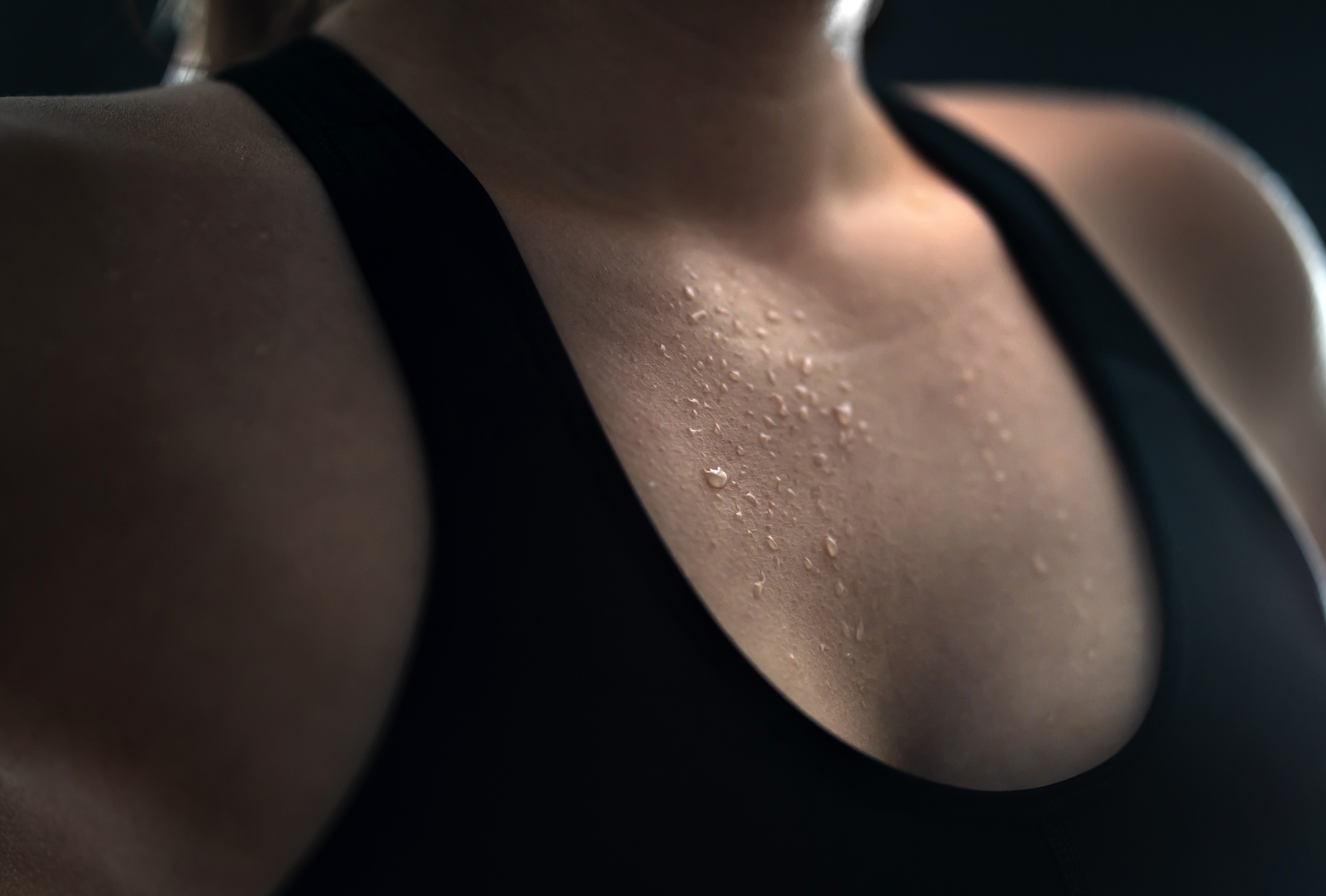 Close-up of a person wearing a sleeveless top with droplets of sweat on their chest, suggesting physical activity or passion