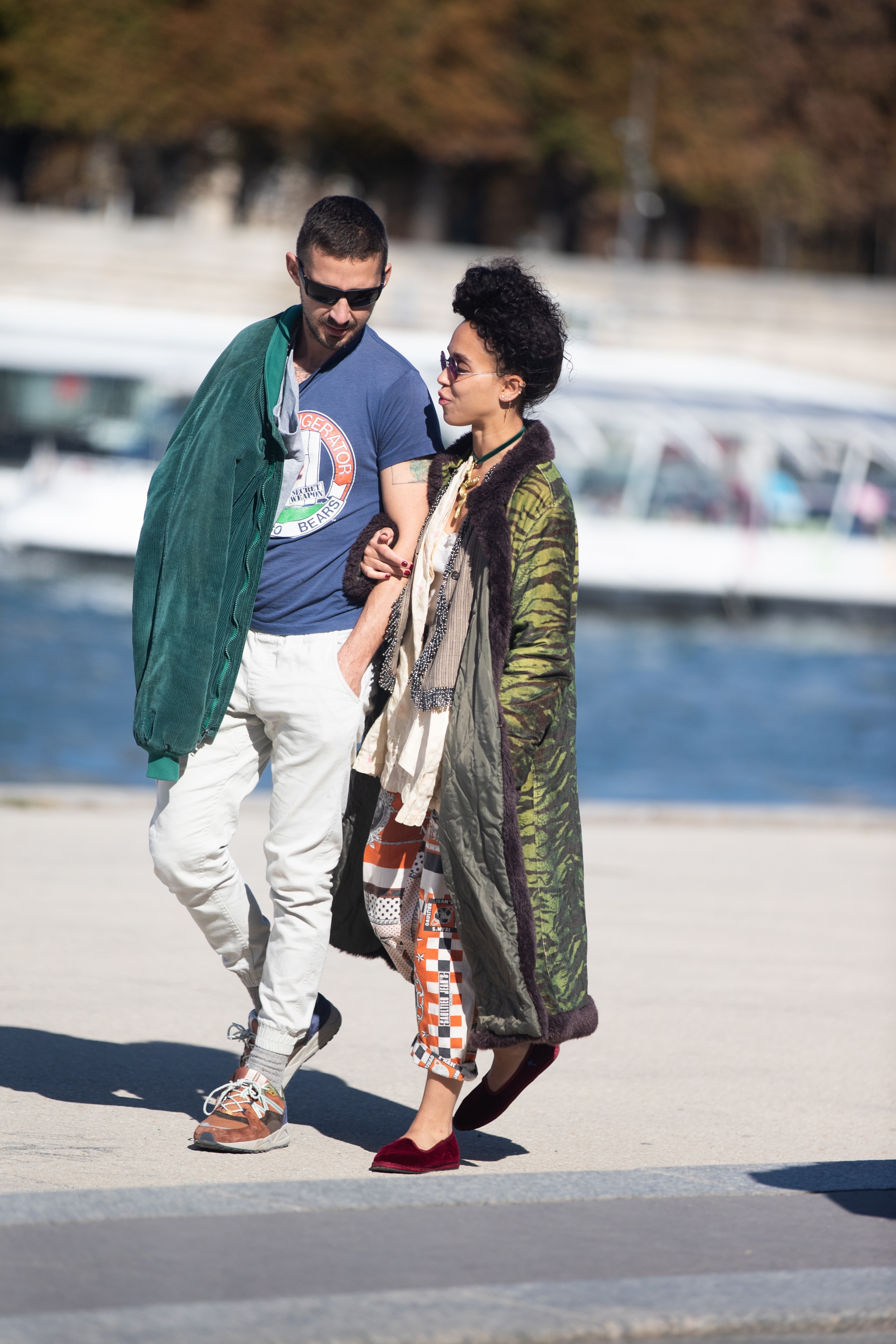 Two individuals walking unneurotic  outdoors; 1  wears a T-shirt and airy  pants, the different   a patterned overgarment  and checkered pants