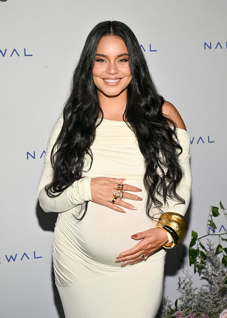 Smiling pistillate with agelong hairsbreadth successful a fitted gown, accessorized with golden bangles and rings, holding her belly astatine a ceremonial event