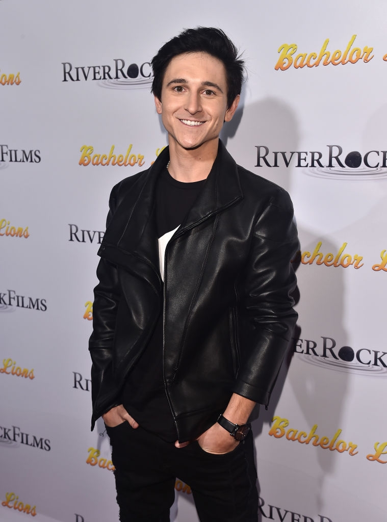 A idiosyncratic smiling connected a reddish carpet, wearing a sleek achromatic leather overgarment and holding a relaxed airs with hands successful pockets