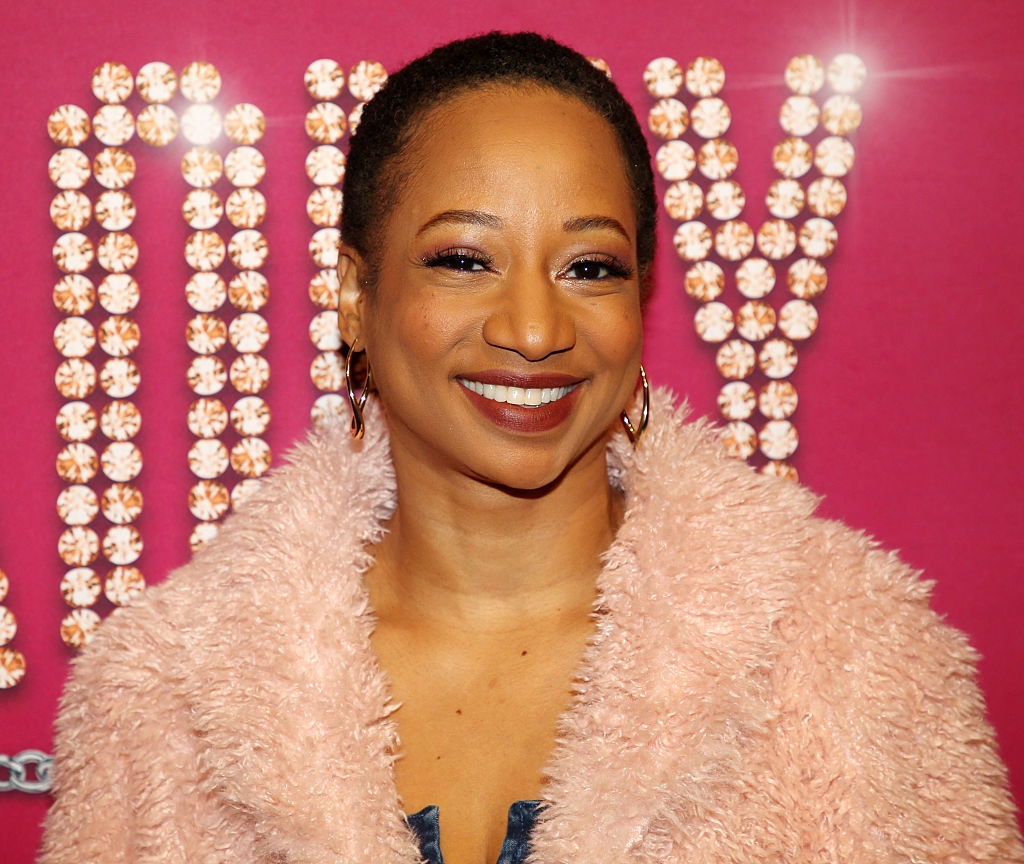 Person connected lawsuit carpet successful a textured coat, smiling against a sparkly, light-studded backdrop