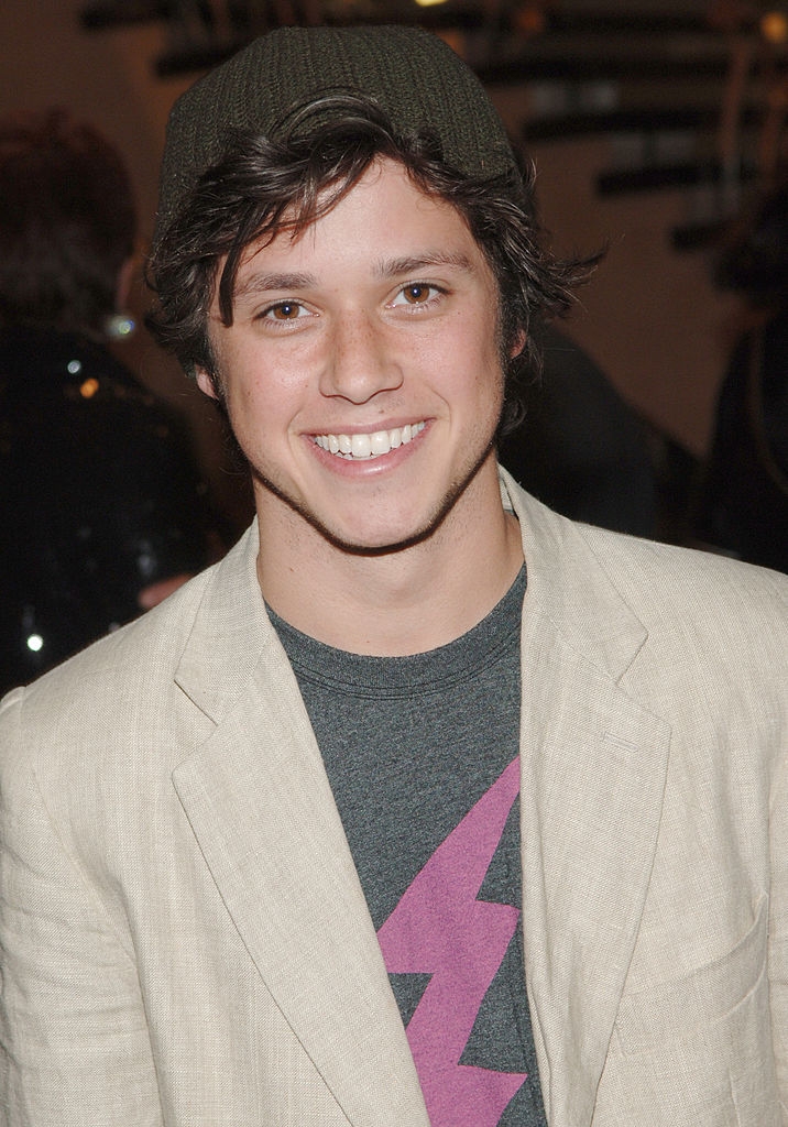 A idiosyncratic wearing a blazer, graphic t-shirt with a lightning bolt, and a beanie, smiling astatine an event