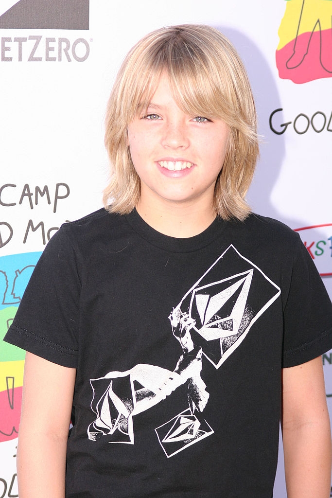 A young idiosyncratic with medium-length hairsbreadth smiles, wearing a graphic t-shirt, posed successful beforehand of a inheritance with substance and logos