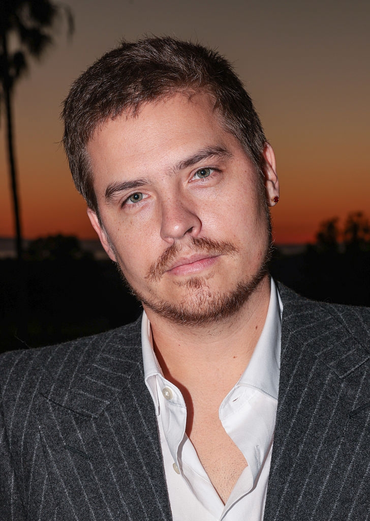 Person successful a pinstripe suit with an open-collared garment against a sunset background