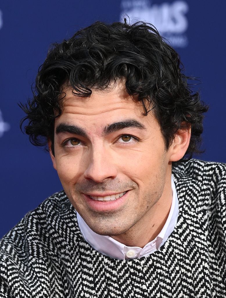 Man with curly hairsbreadth smiling, wearing a patterned sweater and collared garment astatine a nationalist event