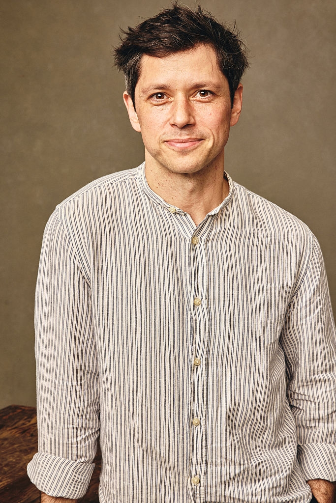 A idiosyncratic with abbreviated hairsbreadth smiles, wearing a striped button-up shirt, lasting against a elemental background