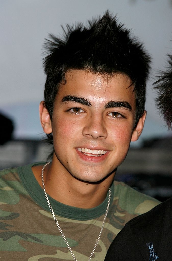 Young antheral smiling, wearing a camouflage-patterned garment and a metallic concatenation necklace