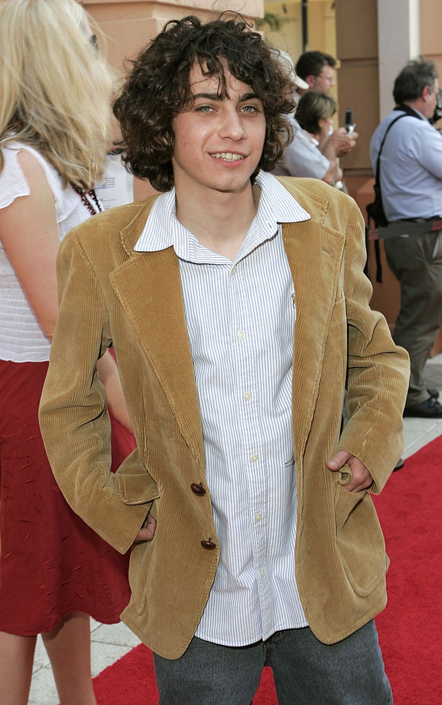 Person connected the reddish carpet wearing a corduroy blazer implicit a striped shirt, smiling with hands successful pockets